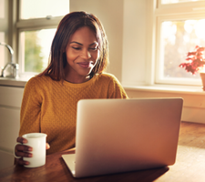 A woman holding a coffee mug and working on a computer.